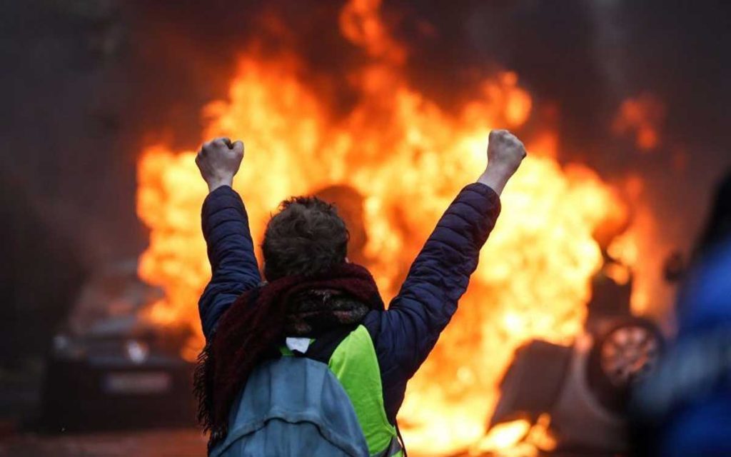 A protester gestures in front of a burning vehicle as "yellow vests" (Gilets jaunes) protesters demonstrate against rising oil prices and living costs in Paris. 