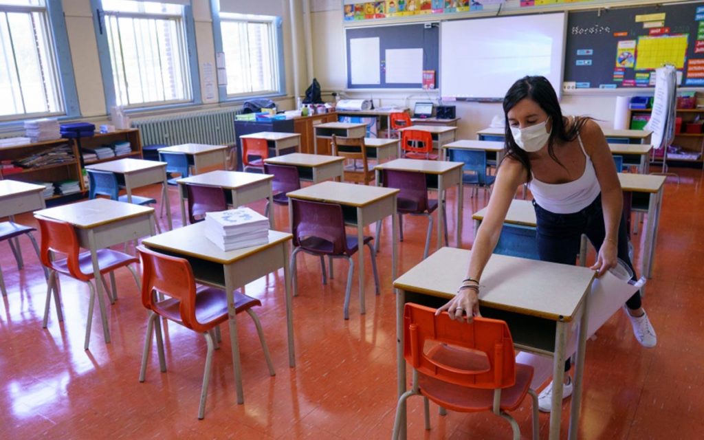 teacher wiping down desks in a classroom