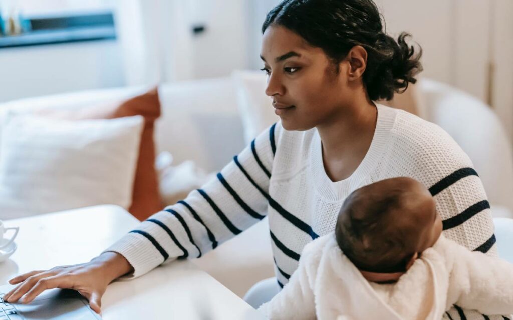 a person holding a baby and working on their laptop