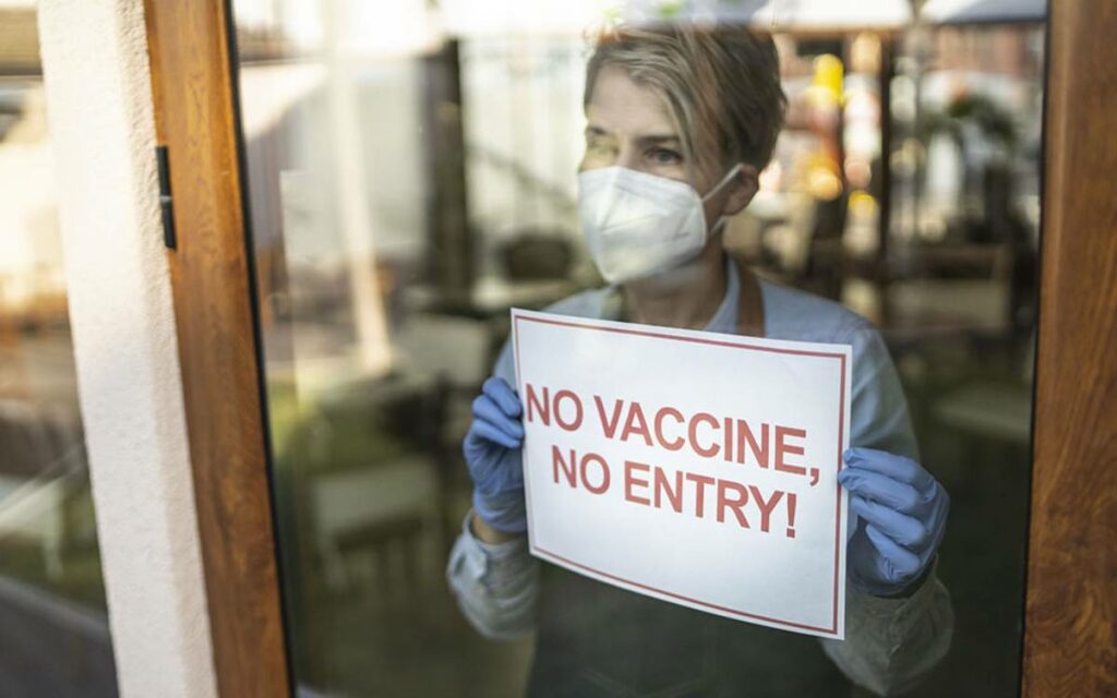 person in a door with a no vaccine, no entry sign